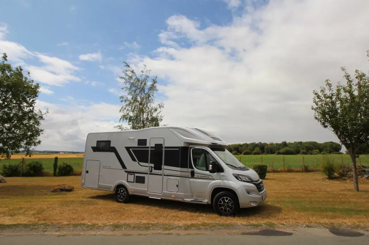 Camping-car Adria Matrix 670 SC argenté, stationné dans un champ sous un ciel nuageux.