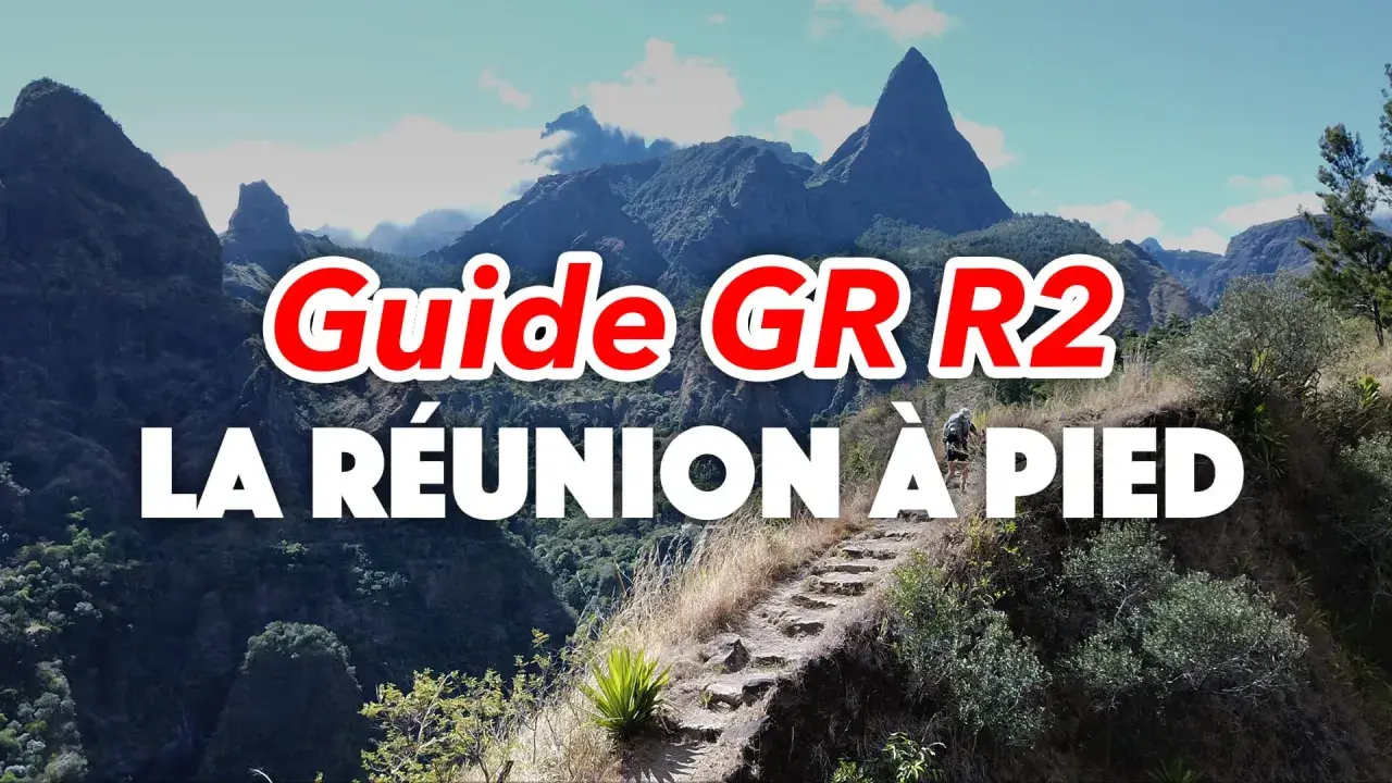 Guide GR R2 : La Réunion à pied, un randonneur sur un sentier escarpé avec des montagnes majestueuses en arrière-plan.