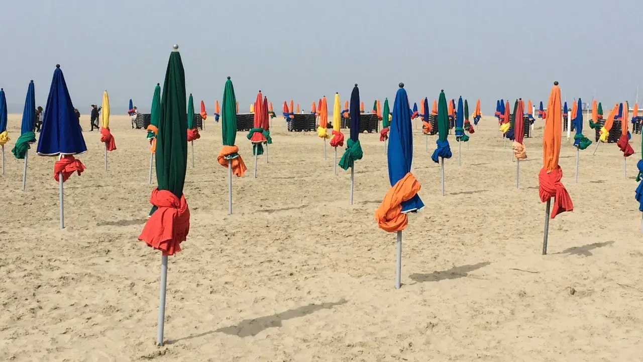 Des parasols colorés, bleus, verts, rouges et jaunes, sont alignés sur la plage de Deauville, prêts à accueillir les visiteurs.