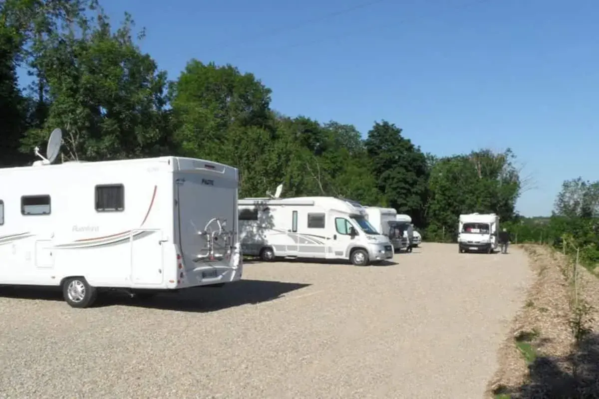 Stationnement de camping-cars sous un ciel bleu, avec des arbres en arrière-plan. Une aire camping car Arras paisible pour les voyageurs.