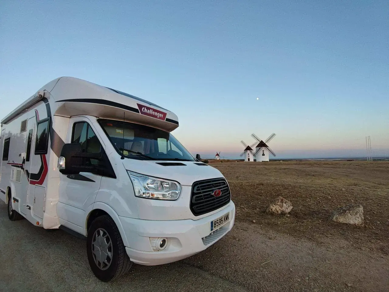 Un camping-car blanc est garé devant des moulins à vent au coucher du soleil. Un voyage en camping-car inoubliable.