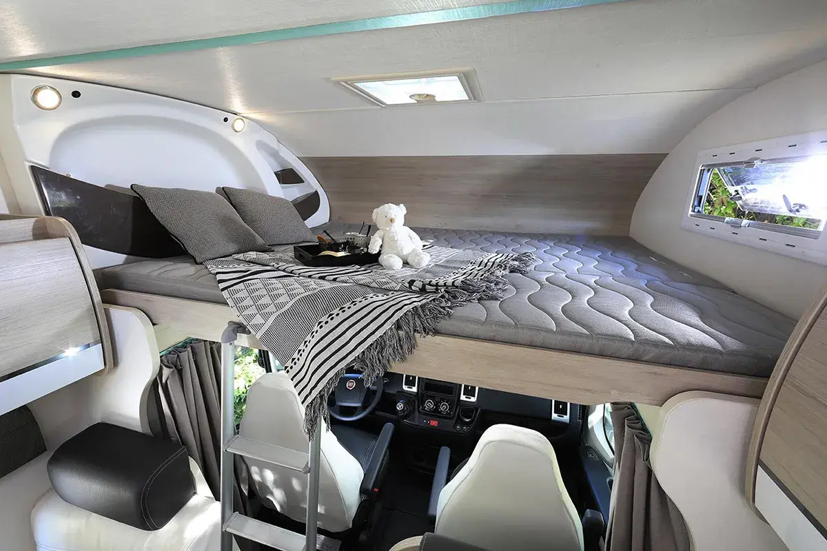 Lit pavillon confortable dans un camping-car, prêt pour une nuit paisible. Un ours en peluche veille sur le sommeil.