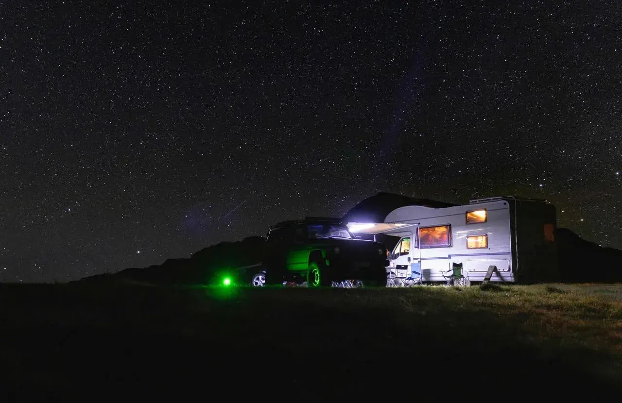 Un camping-car et un 4x4 illuminés sous un ciel étoilé. L'endroit parfait où dormir en camping-car pour admirer la voie lactée.