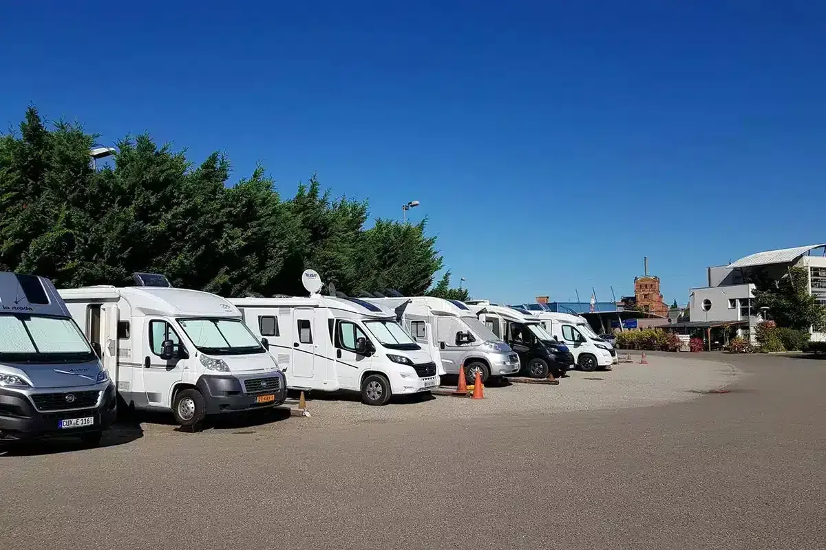 Rangée de camping-cars blancs et gris garés sous un ciel bleu clair.