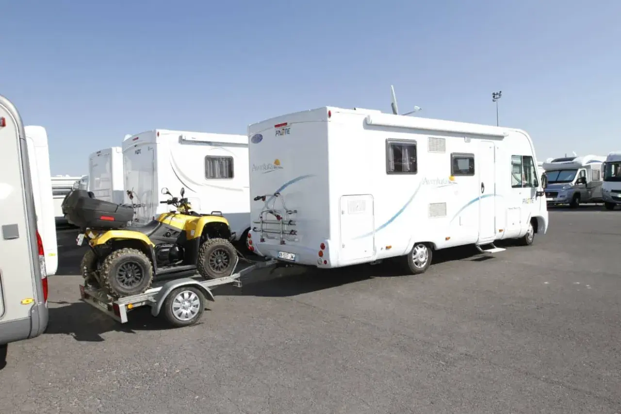 Un quad jaune sur une remorque, prêt à être tracté par un camping-car. Le quad est bien attaché, prêt pour l'aventure, comme indiqué sur la carte grise.