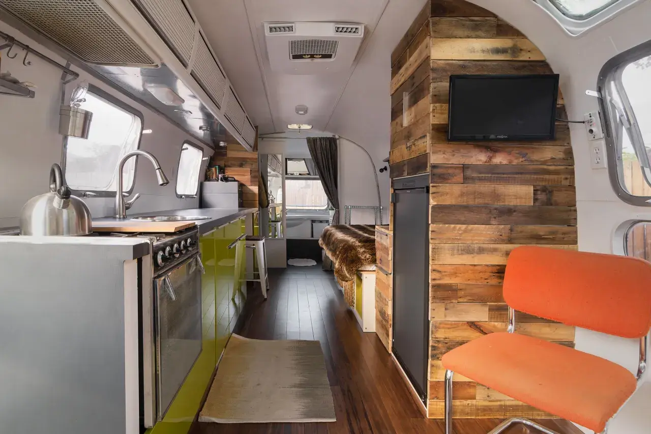 Intérieur d'une caravane Airstream rénovée, avec cuisine, lit douillet et mur en bois rustique.