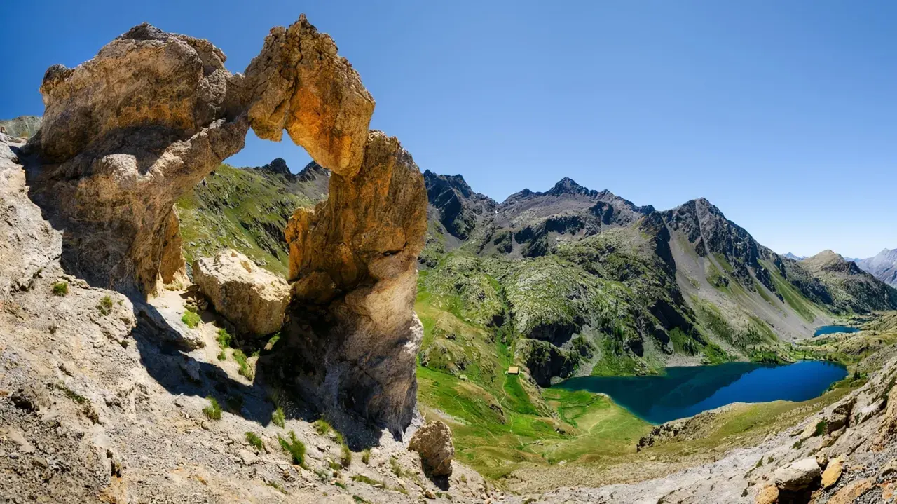 Un arc rocheux spectaculaire domine un paysage de montagne verdoyant, avec des lacs bleus scintillants. Une vue digne d'une carte du Mercantour.
