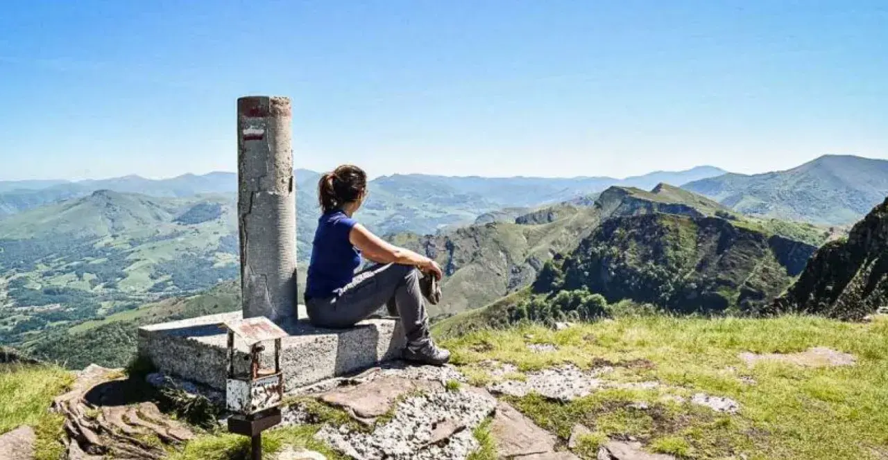 Vue panoramique sur les montagnes verdoyantes du gr pays basque. Une randonneuse contemple le paysage depuis un sommet.