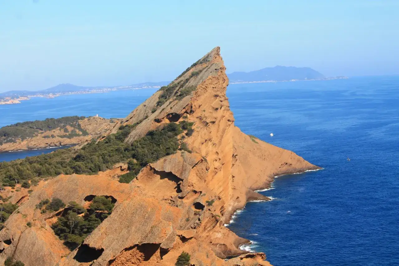 Le Bec de l'Aigle à La Ciotat, un promontoire rocheux aux teintes ocre, plonge dans la mer d'un bleu profond. Des pins maritimes s'accrochent aux pentes.