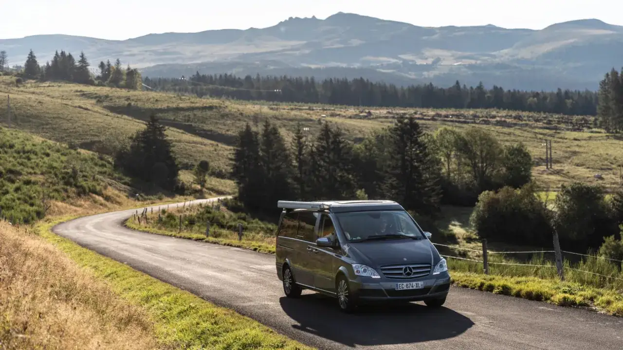 Camping-car Mercedes sur une route sinueuse en Auvergne, paysage vallonn&eacute; et verdoyant. Une aire de camping-car gratuite vous attend !