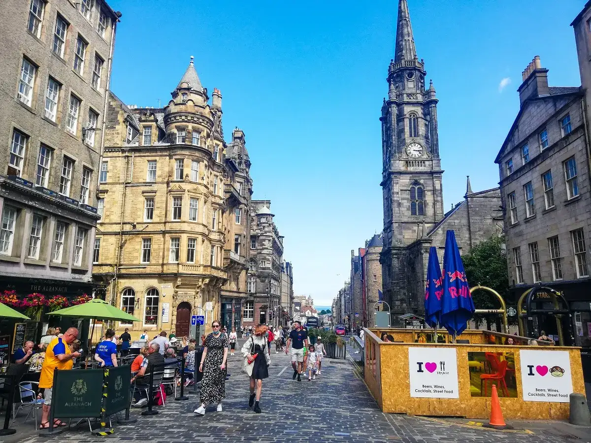 Une rue animée à Édimbourg, avec des bâtiments historiques, une église imposante et des terrasses de cafés. Idéal pour savoir que faire à Édimbourg.