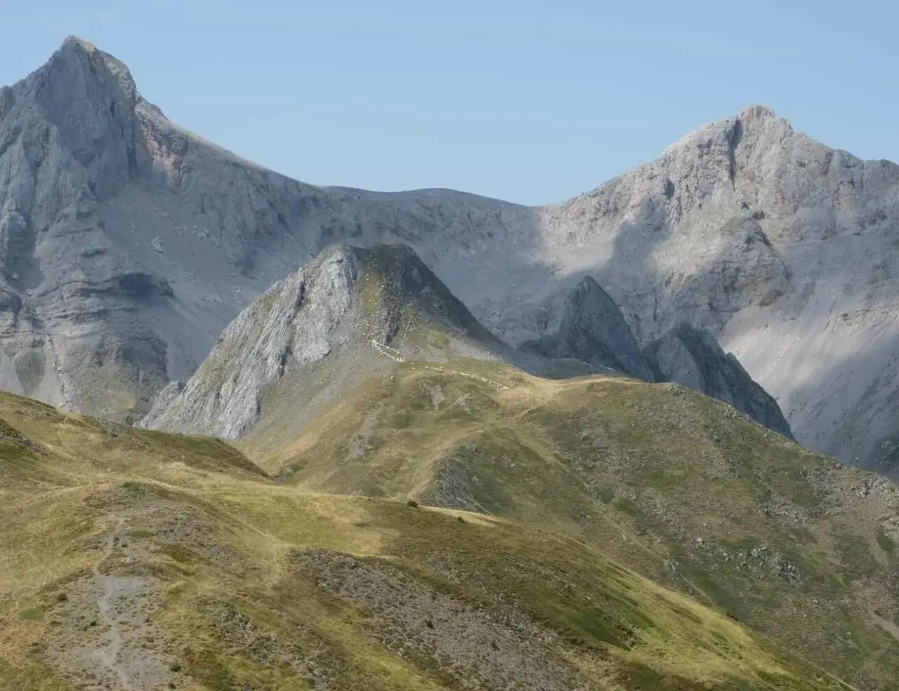 Chemin de randonnée menant au lac d'Ansabère, traversant des prairies verdoyantes et des pentes rocheuses où paissent des moutons.