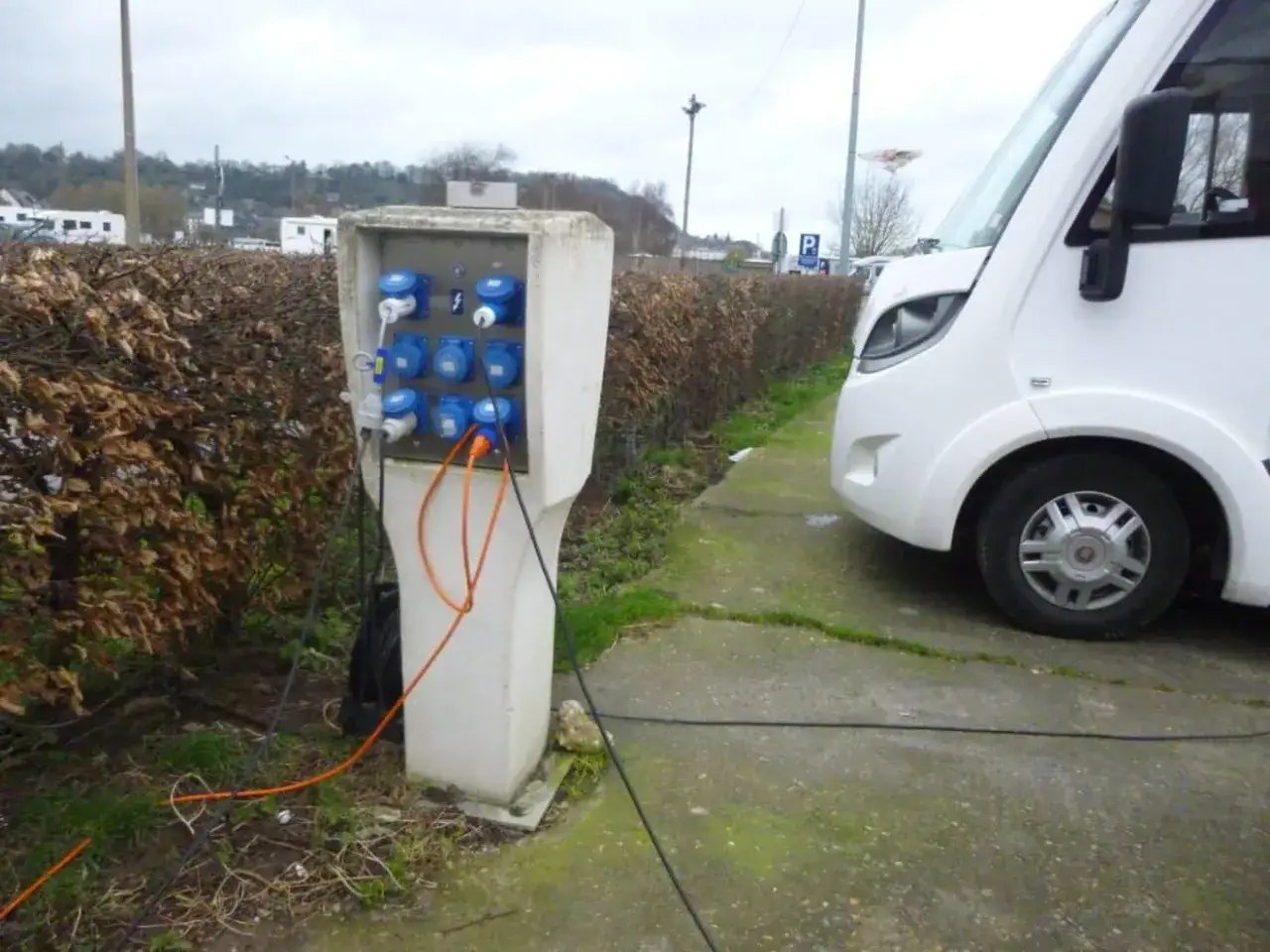 Borne électrique pour camping-car, offrant une aire de camping-car gratuit avec électricité. Un camping-car blanc est garé à côté.
