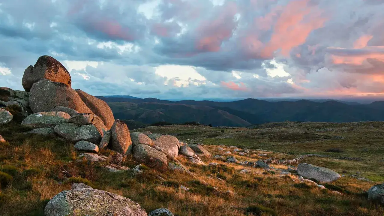 Gros rochers sur un plateau herbeux, sous un ciel aux teintes rosées. Un paysage qui invite à la randonnée sur le chemin de Stevenson 4 jours.