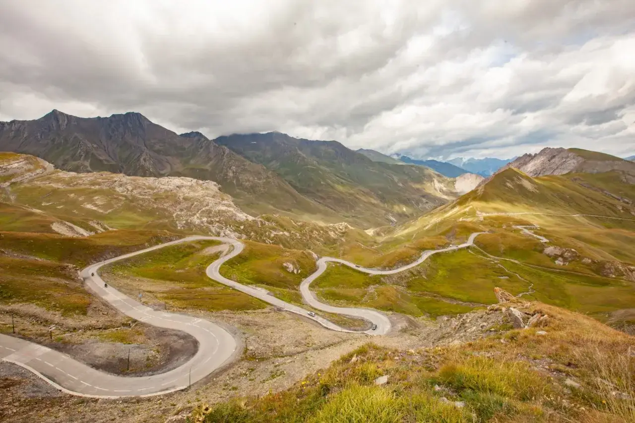 La route des Grandes Alpes en voiture serpente à travers des montagnes verdoyantes sous un ciel nuageux. Un paysage spectaculaire pour une aventure inoubliable.