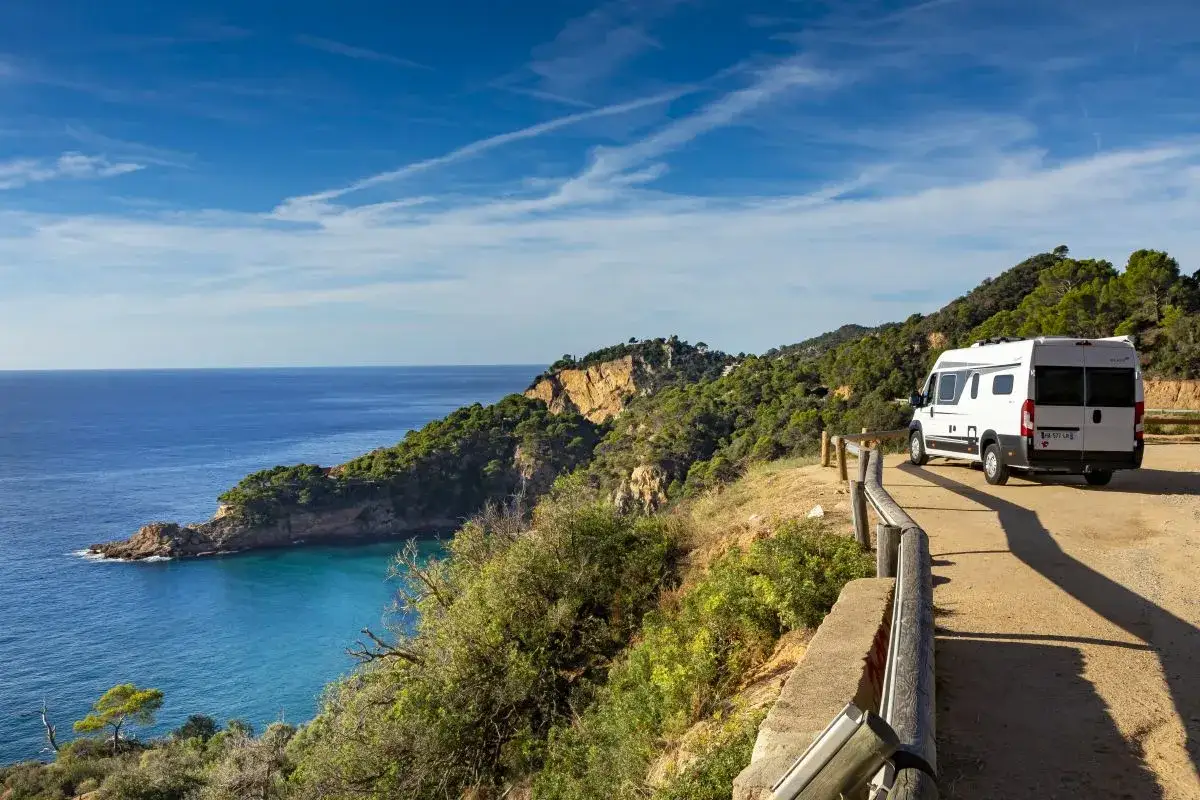 Un camping-car blanc profite d'une vue imprenable sur la mer Méditerranée et les falaises verdoyantes de la Costa Brava.