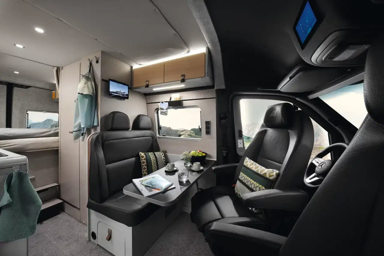 Intérieur d'un camping-car baroudeur confortable avec banquette, table, lits superposés et vue sur la montagne.