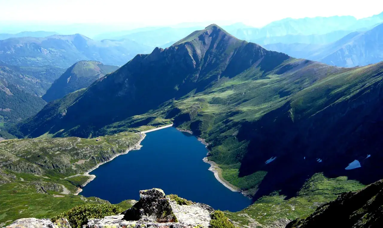 Vue panoramique depuis le tour du Biros sur un lac bleu profond niché au creux de montagnes verdoyantes.