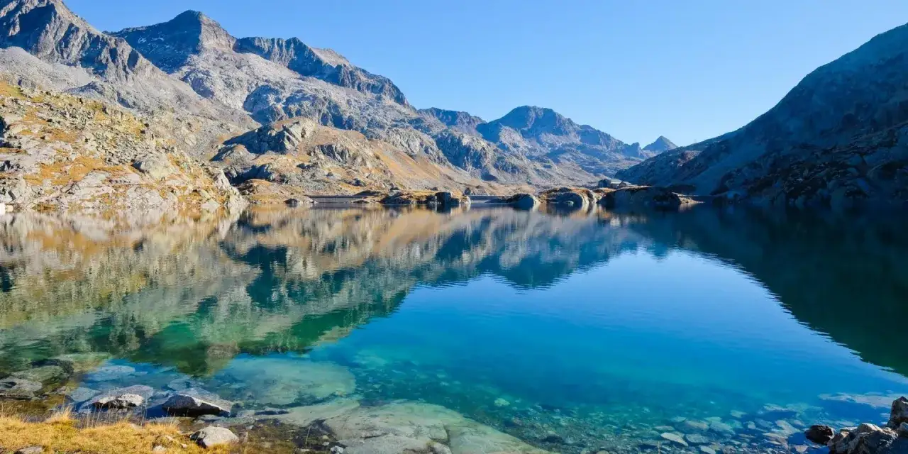 Lac d'altitude aux eaux turquoise, reflétant les montagnes rocheuses du massif de Belledonne. Une carte naturelle de sérénité.