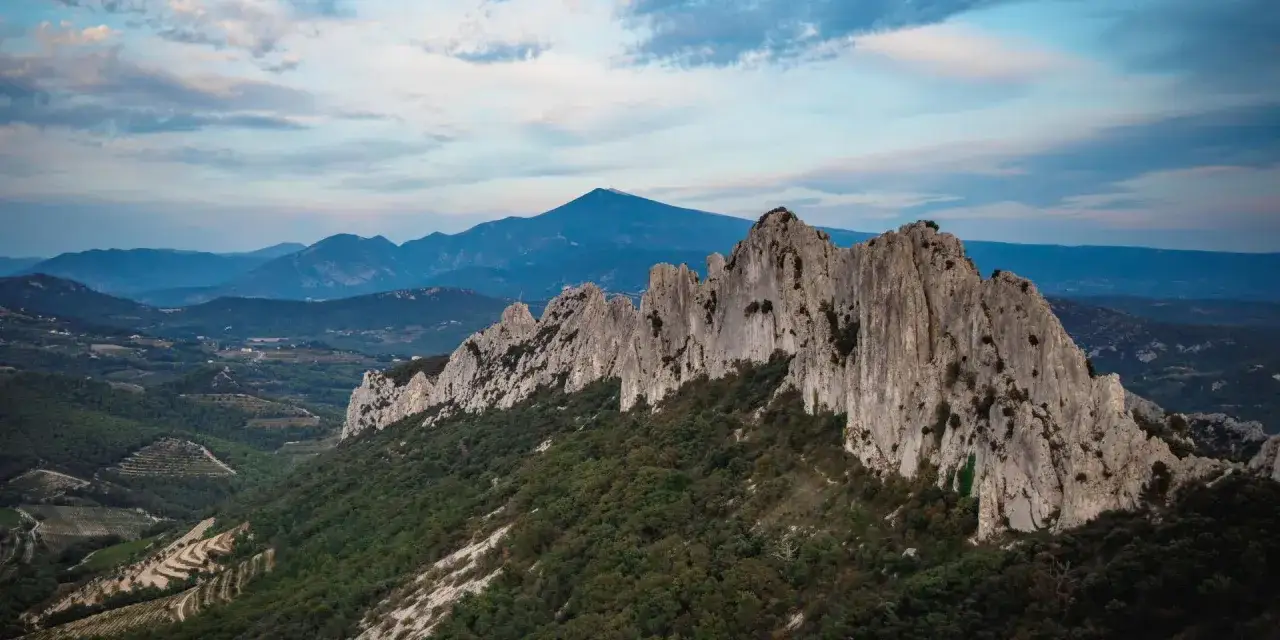 Les dentelles de Montmirail, un paysage spectaculaire de roches escarpées et de montagnes bleutées sous un ciel nuageux.