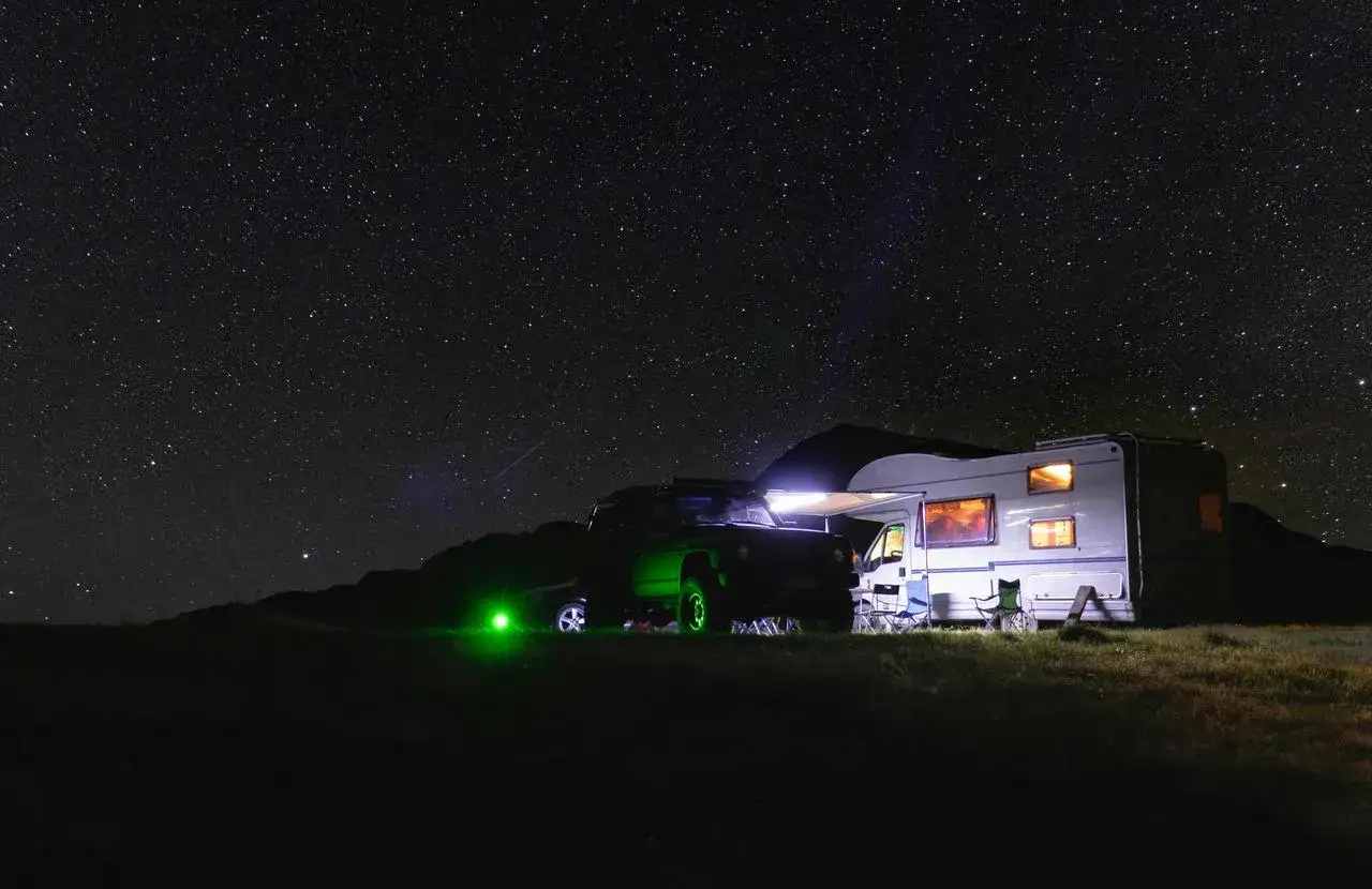 Un camping-car et un 4x4 illumin&eacute;s sous un ciel &eacute;toil&eacute;. L'endroit id&eacute;al o&ugrave; dormir en camping-car pour admirer la voie lact&eacute;e.