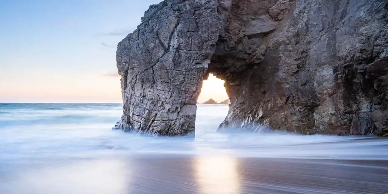 Une arche rocheuse sur la côte, parfaite pour une randonnée à pied sur la presqu'île de Quiberon. L'eau caresse le sable dans un doux mouvement.