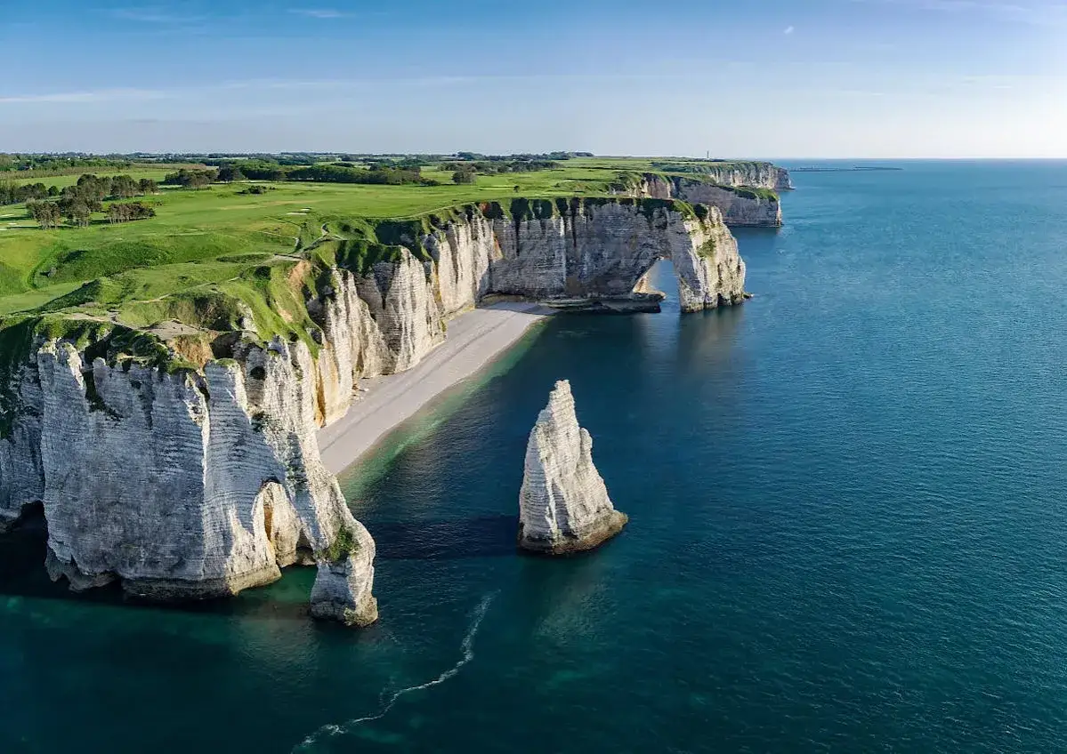 Falaises d'Étretat, un parcours de golf verdoyant surplombe la mer d'un bleu profond. Les arches naturelles et le rocher Aiguille marquent les étapes du GR21.