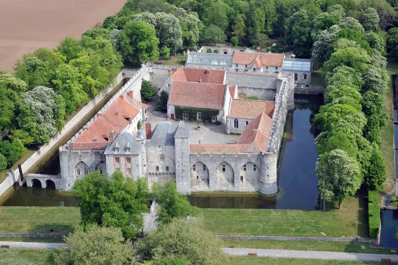 Vue a&eacute;rienne du ch&acirc;teau de Farcheville, entour&eacute; de douves et de verdure. Les toits rouges contrastent avec les murs de pierre grise.
