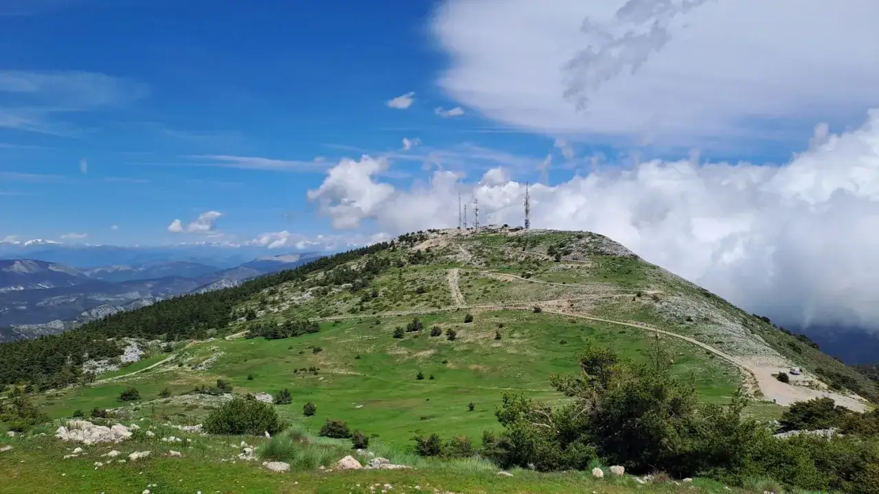 Vue panoramique du mont Lachen, avec ses antennes de télécommunication au sommet, ses pentes verdoyantes et le ciel bleu parsemé de nuages.