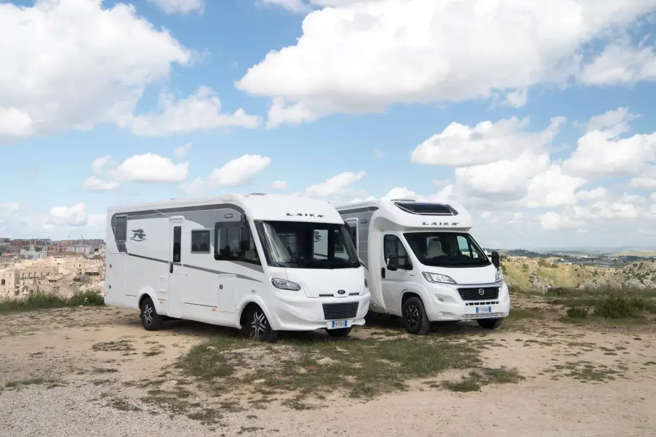 Deux camping-cars blancs Laika stationnés sur un terrain rocailleux, avec une ville en arrière-plan. Idéal pour savoir comment choisir son camping-car.