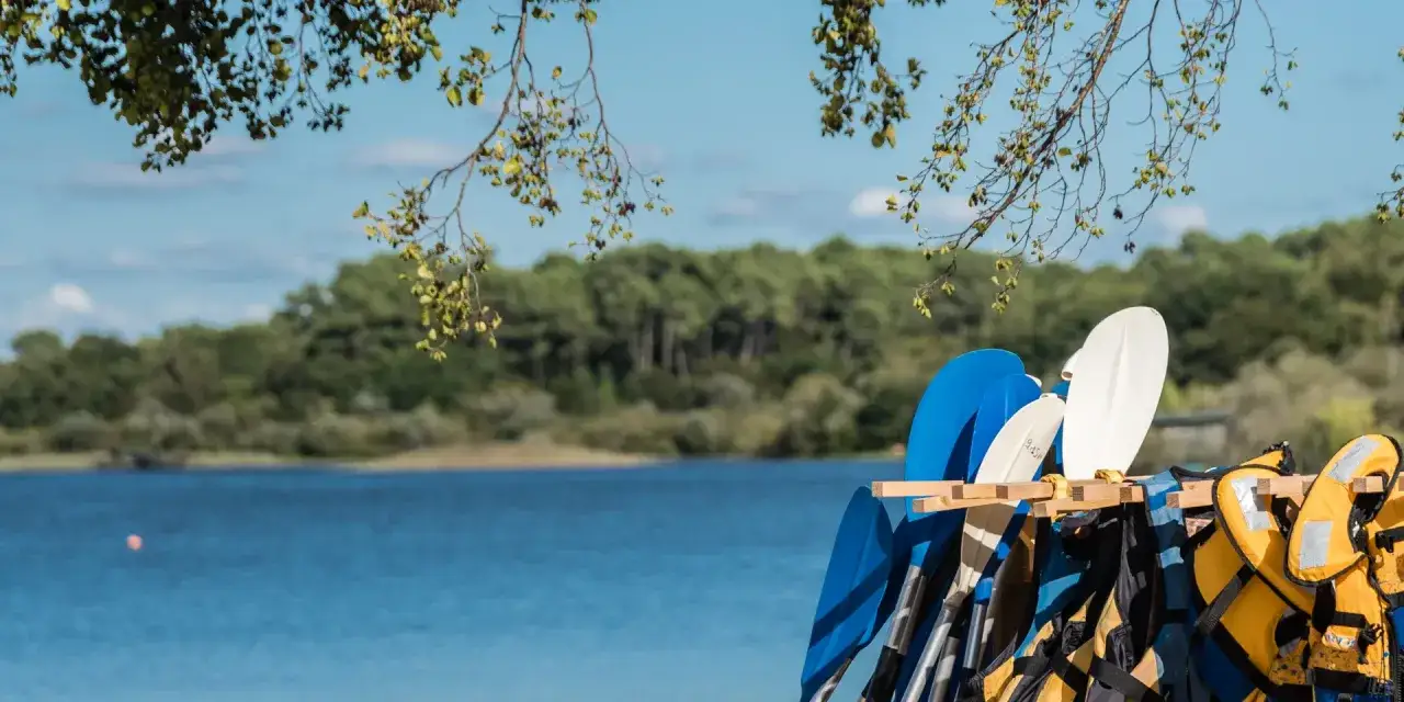 Pagaies bleues et blanches pr&ecirc;tes pour une aventure sur le lac d'Aureilhan, avec des gilets de sauvetage jaunes &agrave; proximit&eacute;.