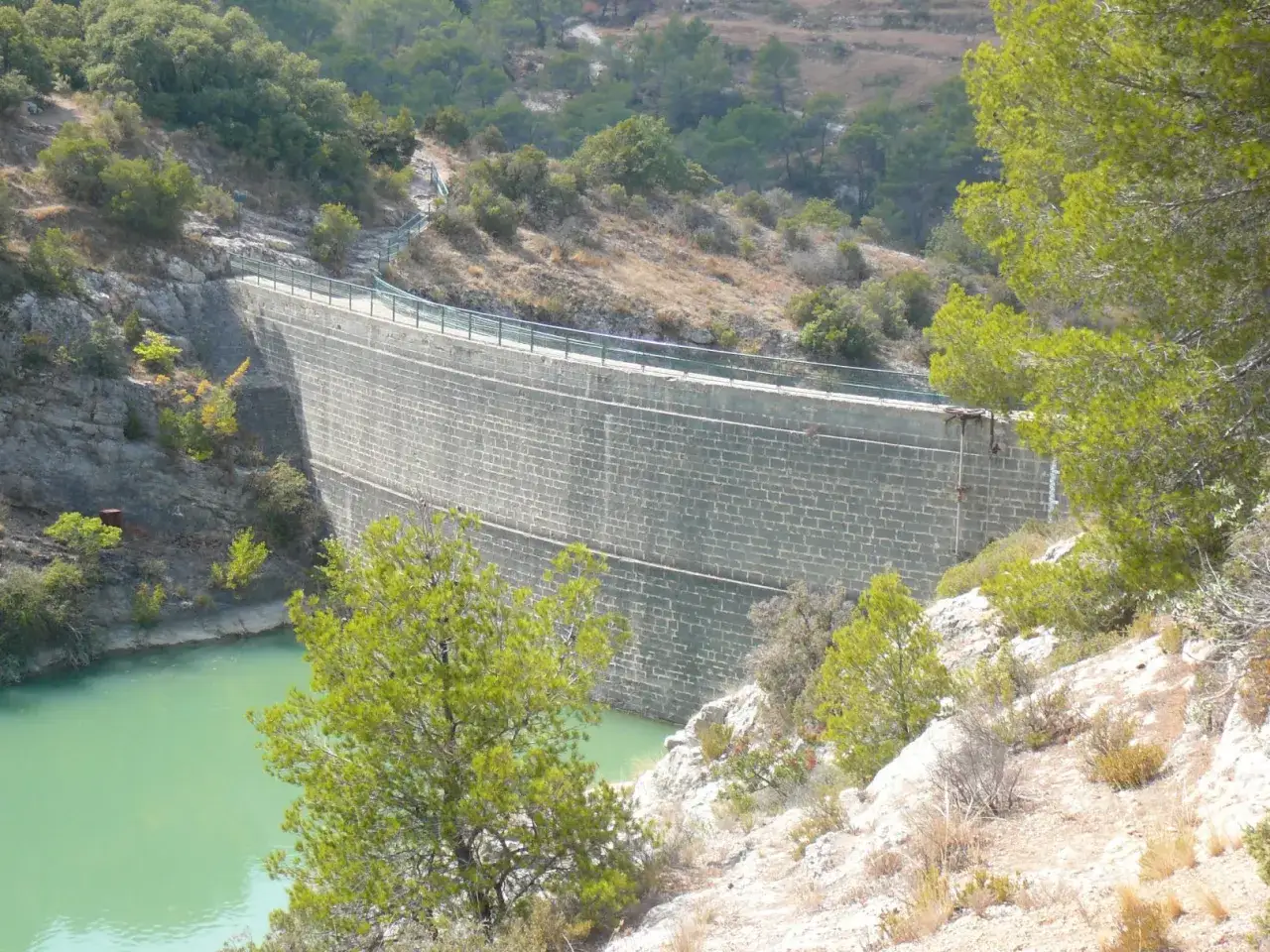 Barrage imposant retenant les eaux turquoise du lac Zola, entour&eacute; de v&eacute;g&eacute;tation m&eacute;diterran&eacute;enne.