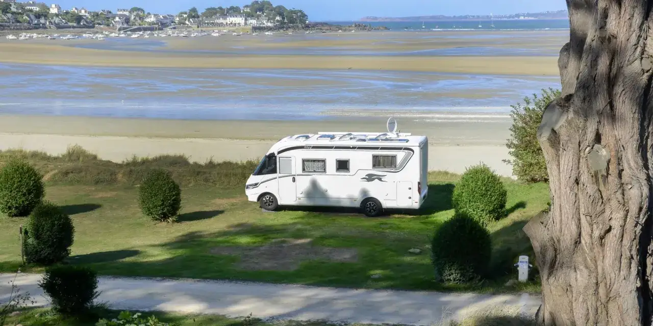 Camping-car blanc garé sur une aire de camping-car gratuite en bord de mer en Bretagne. Vue sur la plage et le village au loin.