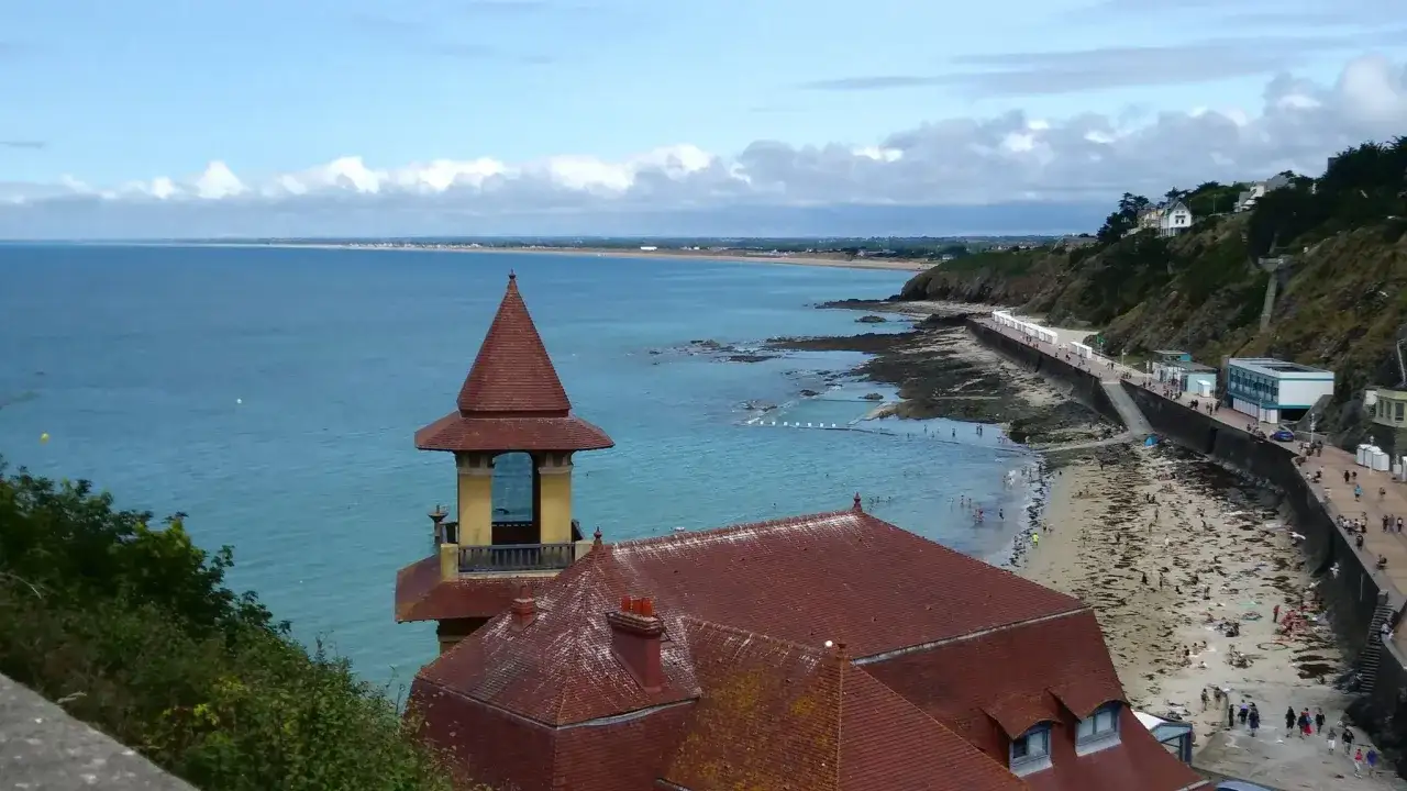 Vue sur la plage de Granville, avec une tour et des toits rouges au premier plan. Idéal pour une randonnée Granville.