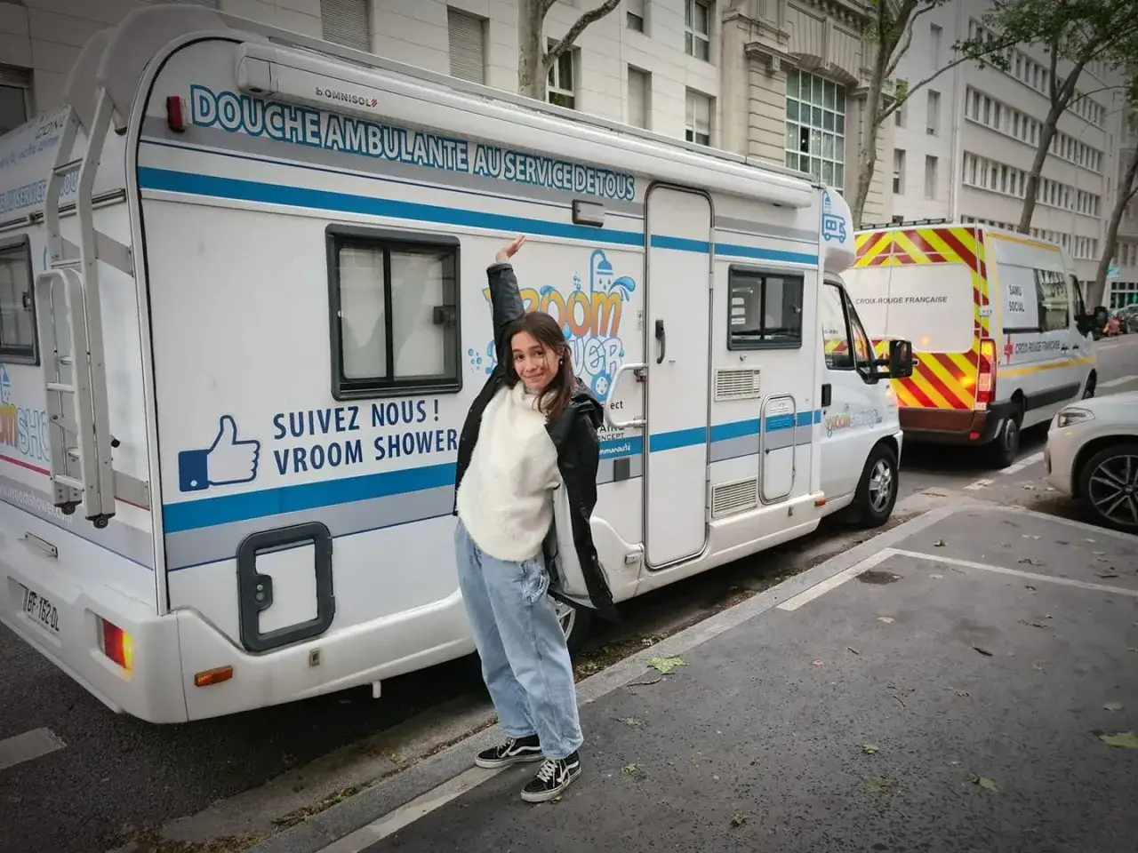 Une jeune femme pose devant une aire de camping-car avec sanitaire, un Vroom Shower ambulant.