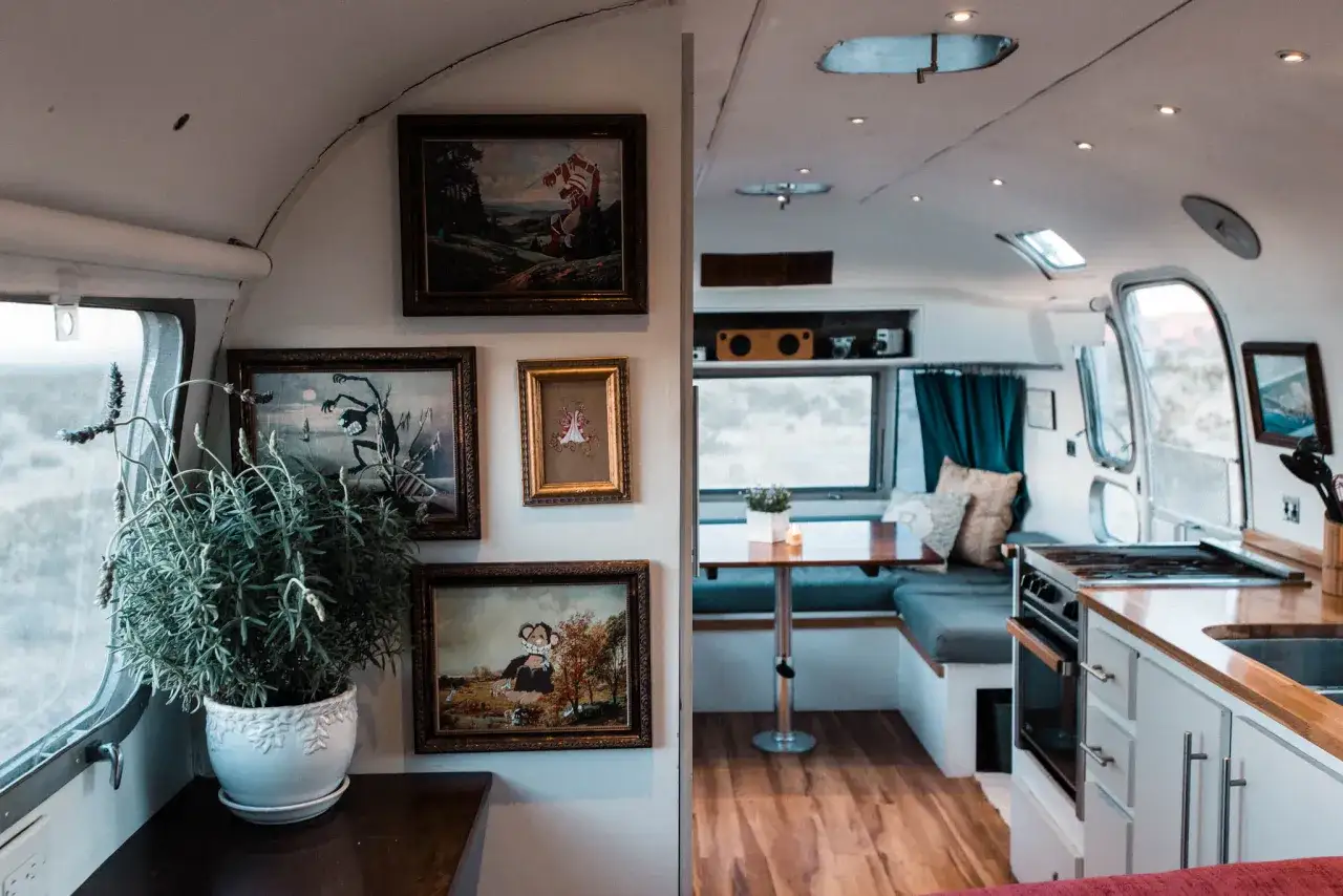 Intérieur d'une caravane Airstream cosy, avec des tableaux accrochés au mur, une plante verte et une cuisine aménagée.