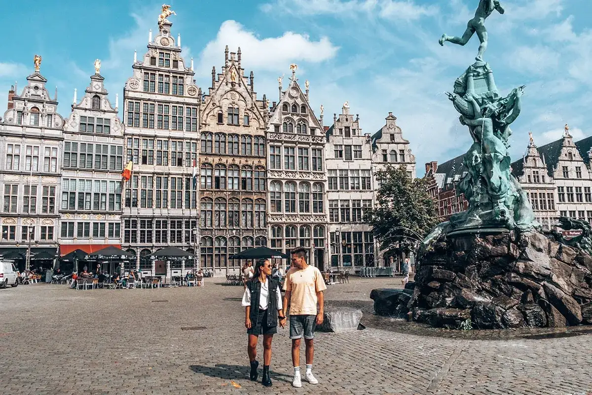 Couple se promène sur la Grand-Place d'Anvers, admirant les façades historiques et la fontaine Brabo. Une belle journée pour visiter Anvers.