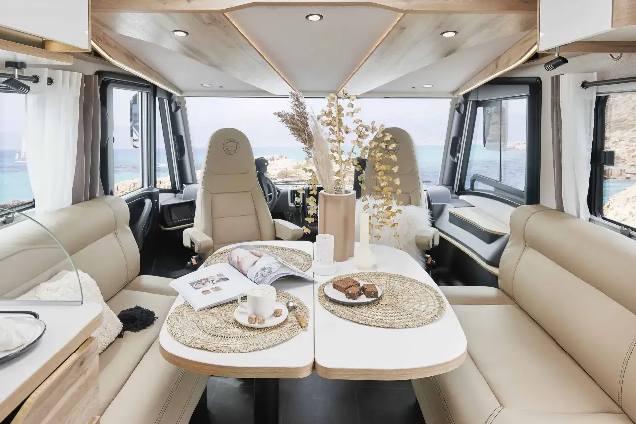 Intérieur d'un camping-car Le Voyageur avec vue sur la mer. Table dressée avec café et gâteaux, sièges confortables.