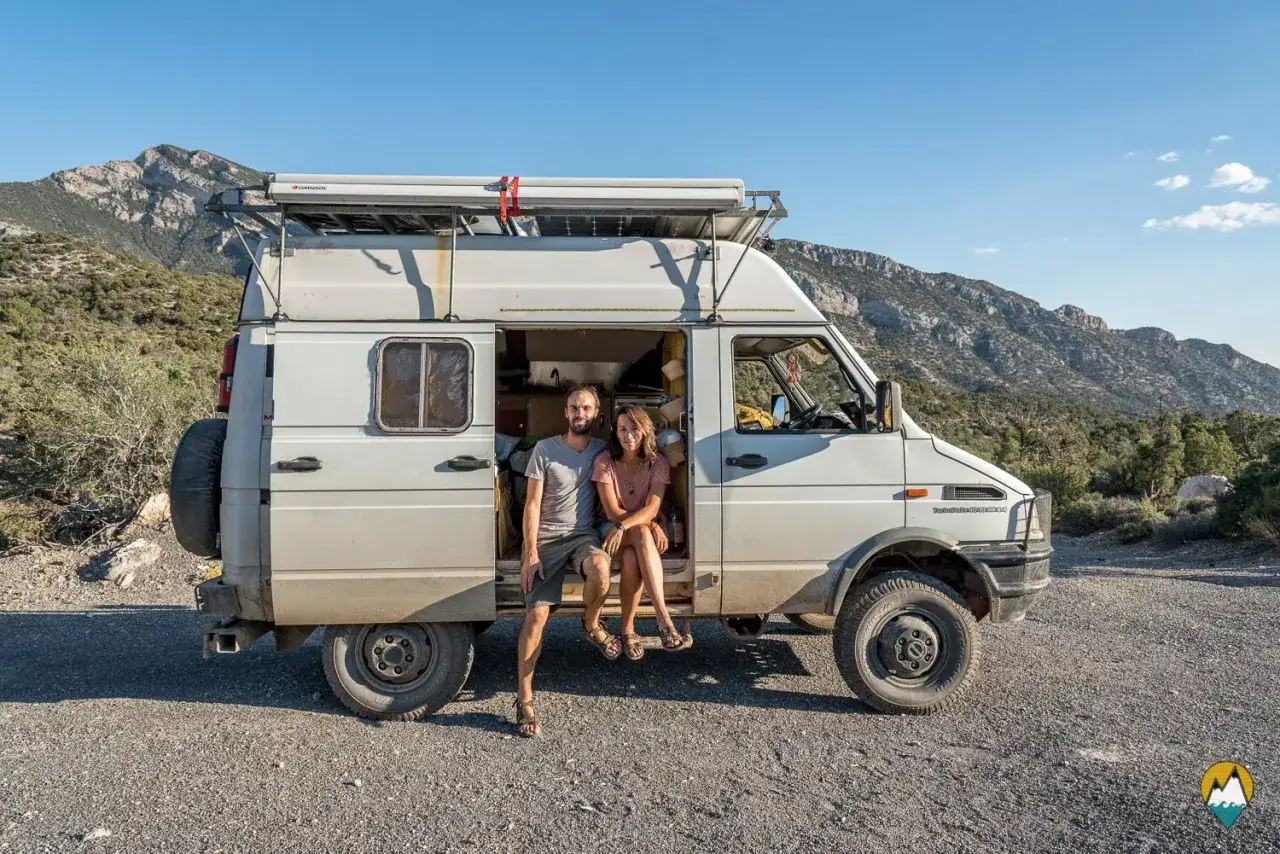 Couple assis &agrave; l'entr&eacute;e d'un fourgon am&eacute;nag&eacute;, pr&ecirc;t pour l'aventure. Ce v&eacute;hicule est l'un des fourgons am&eacute;nag&eacute;s les plus fiables pour explorer les grands espaces.