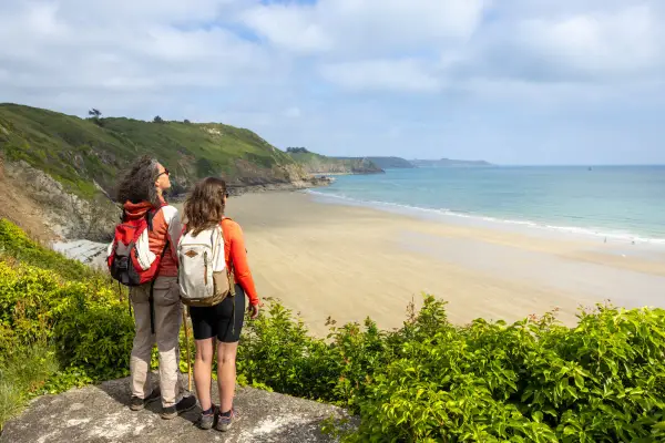 Deux randonneuses contemplent la plage de sable fin et la mer bleue, un paysage typique du GR34 à Saint-Brieuc.